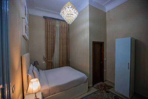 A hotel room with a bed, a nightstand, a lamp, a wardrobe, and a chandelier.