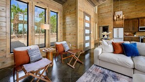 A spacious living area with wooden walls, large windows, a sofa, and a dining table.