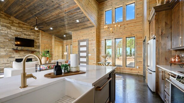 A modern kitchen with wooden walls, a large island, stainless steel appliances, and a ceiling fan.