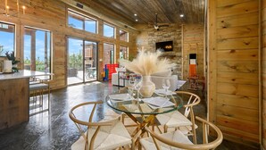 A spacious wooden interior with a glass dining table, chairs, and a kitchen area with a bar.