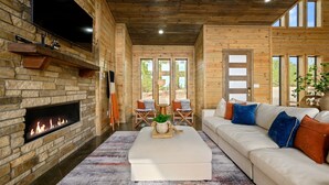 A modern living room with a stone fireplace, a large TV, and a sofa with colorful cushions.