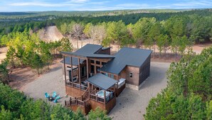 A cabin with a deck, outdoor seating, and a view of the forest.