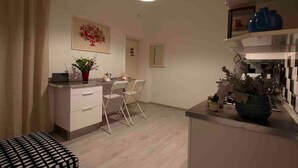 Une cuisine compacte avec un coin repas, comprenant un plan de travail blanc, une plante en pot et un luminaire suspendu.