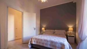 Une chambre à coucher avec un lit, deux tables de chevet avec des lampes, une porte et un grand mur.