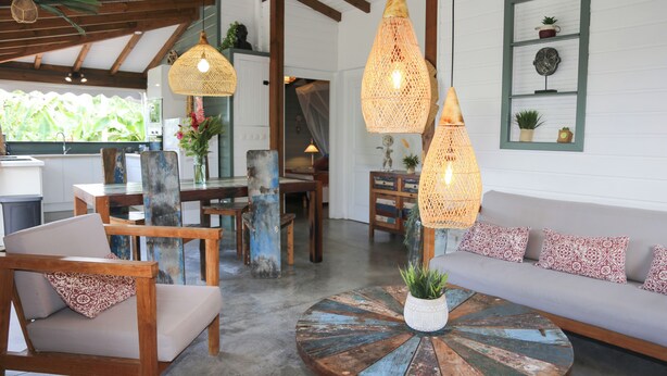 A cozy living room with a round coffee table, wooden chairs, and a sofa. There are hanging wicker lamps and a wall-mounted shelf with plants. - Villa Ô Perchée - swimming pool - panoramic sea view (Pointe-Noire)