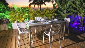 An outdoor dining area with a wooden deck, white chairs, and a table set for four. - Villa Ô Perchée - swimming pool - panoramic sea view (Pointe-Noire)