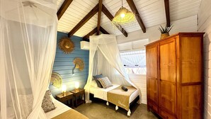 A bedroom with a canopy bed, a wooden wardrobe, and decorative wall hangings. - Villa Ô Perchée - swimming pool - panoramic sea view (Pointe-Noire)