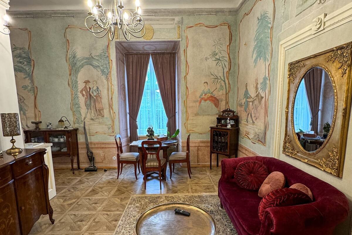 A spacious living room with a chandelier, a red sofa, a dining area, and a large mirror.