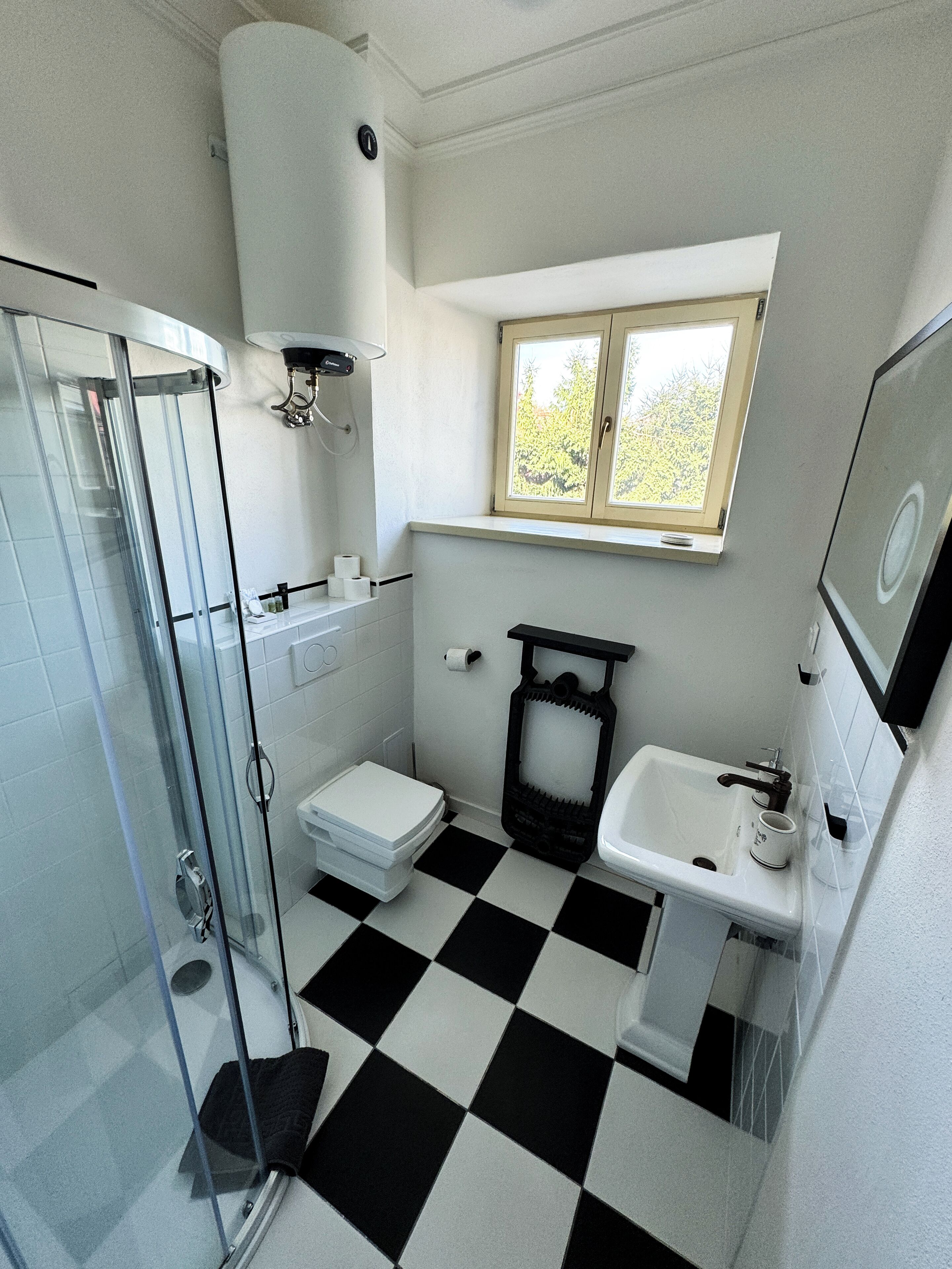 A bathroom with a glass shower enclosure, a toilet, a sink, and a window above the sink.