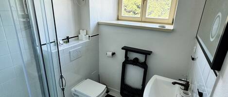 A bathroom with a glass shower enclosure, a toilet, a sink, and a window above the sink.