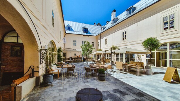 An outdoor courtyard with tables and chairs, a statue, and a fountain. - Opera apartments  (Banska Stiavnica)