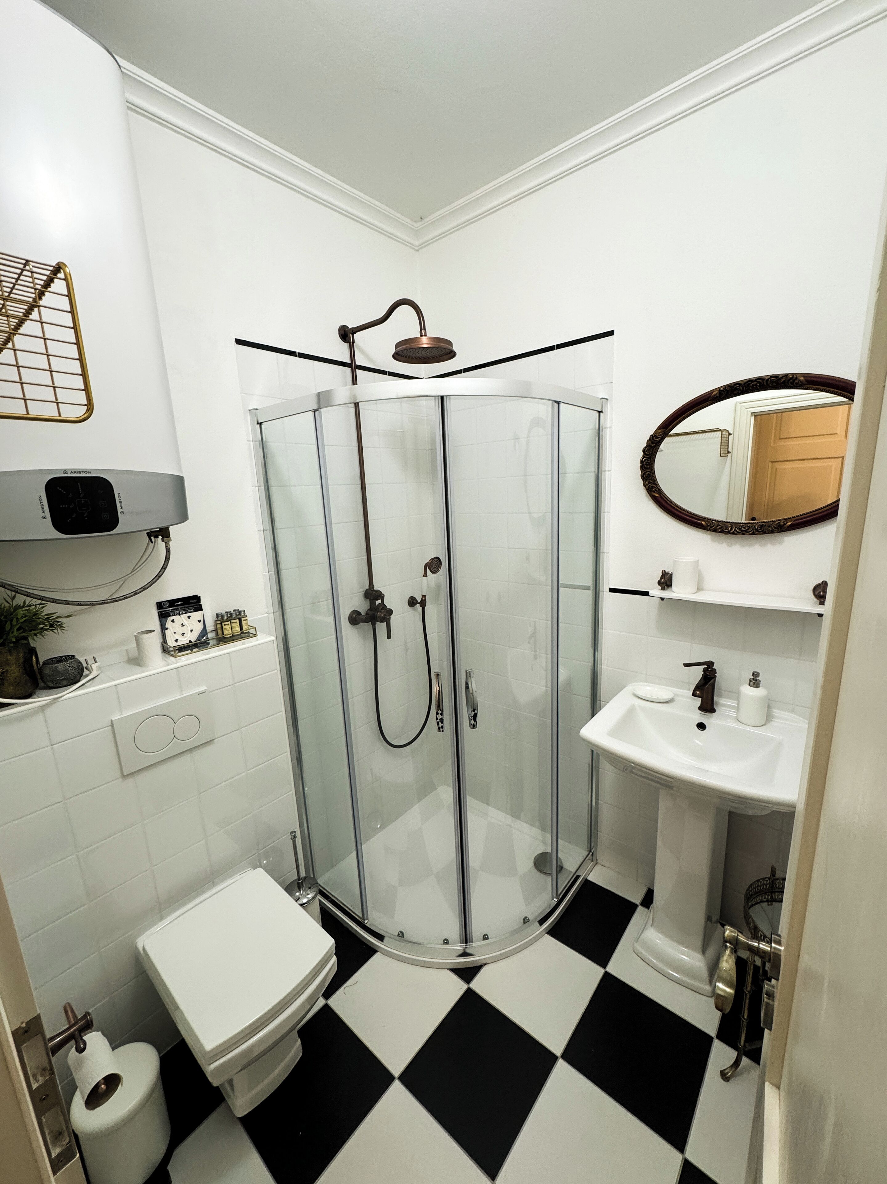 A bathroom with a glass shower enclosure, a white toilet, a sink with a mirror, and a black and white checkered floor.