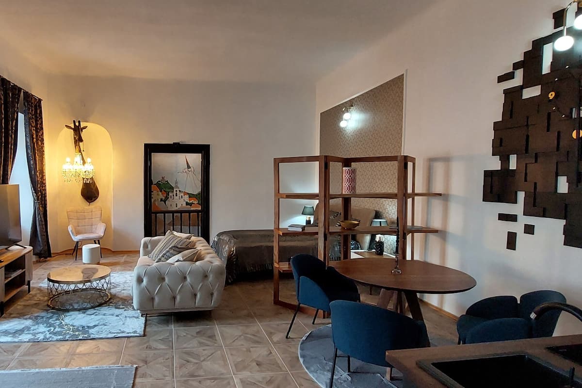 A living room with a sofa, coffee table, and chairs, a dining area with a table and chairs, and a TV on a stand.