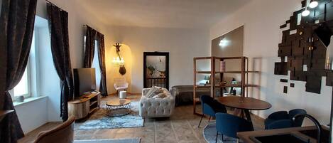 A living room with a sofa, coffee table, and chairs, a dining area with a table and chairs, and a TV on a stand.