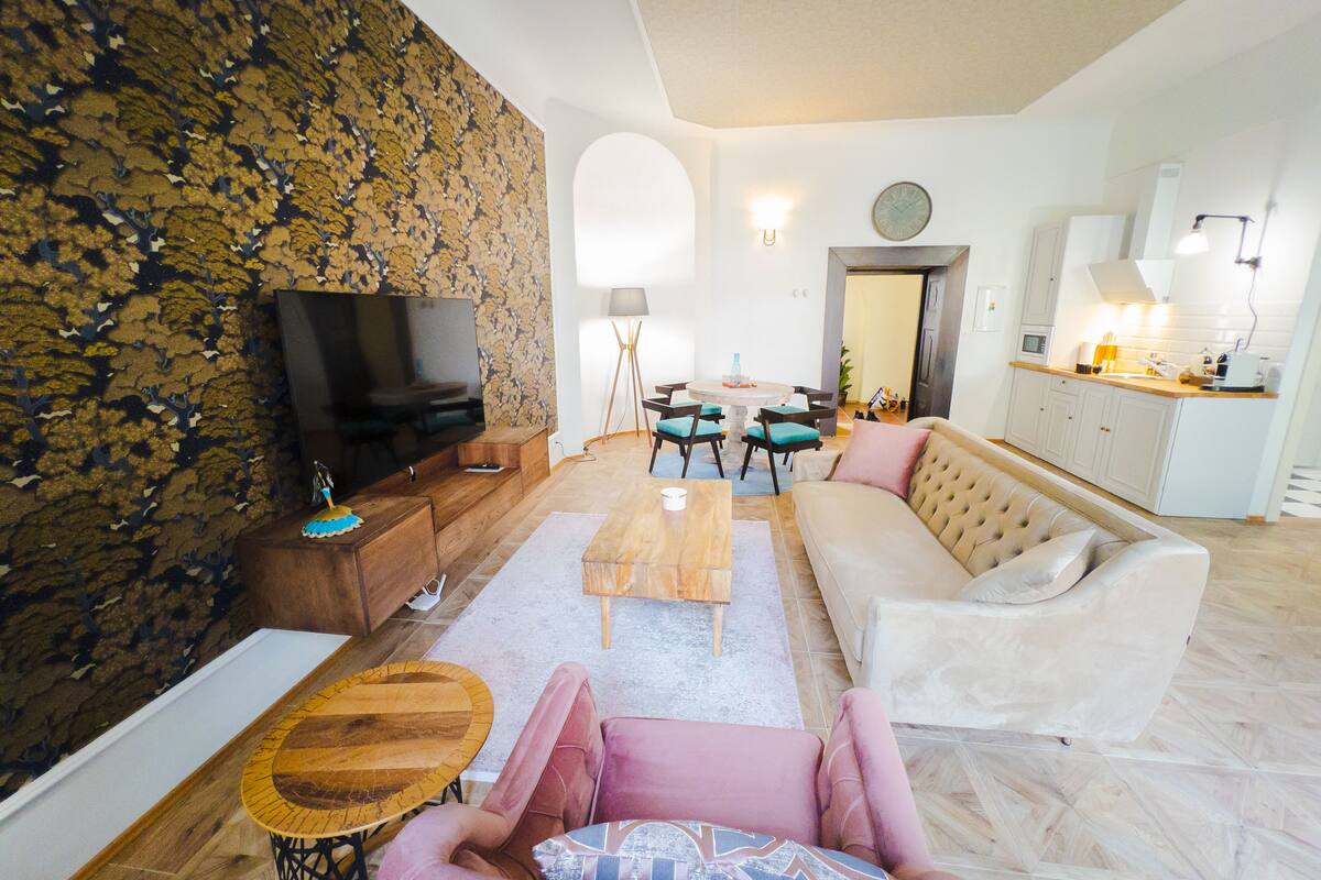 A living room with a television, sofa, coffee table, and a dining area with chairs.