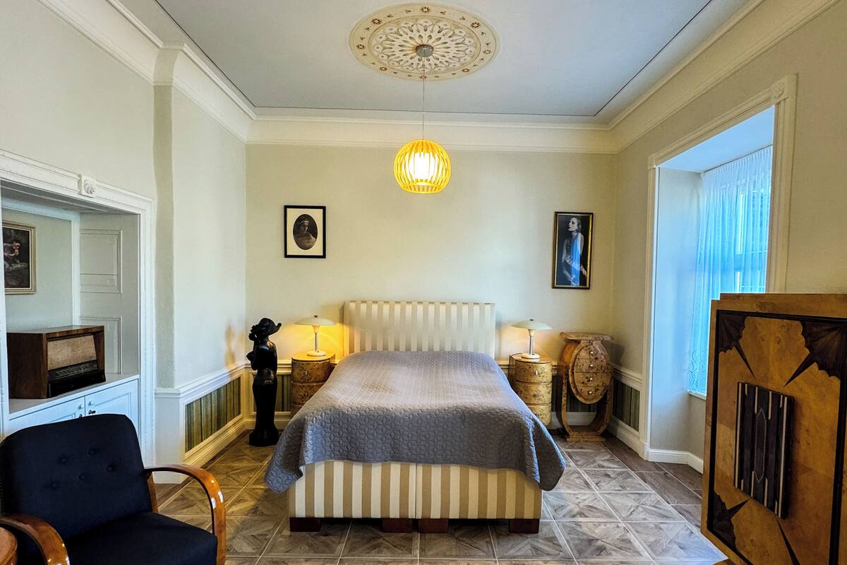 A bedroom with a bed, a chair, a nightstand, a lamp, and a decorative ceiling light.