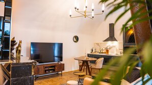 A modern living room with a flat-screen TV, a wooden entertainment unit, a round dining table with chairs, and a kitchen area with a stove and cabinets. - Opera apartments  (Banska Stiavnica)