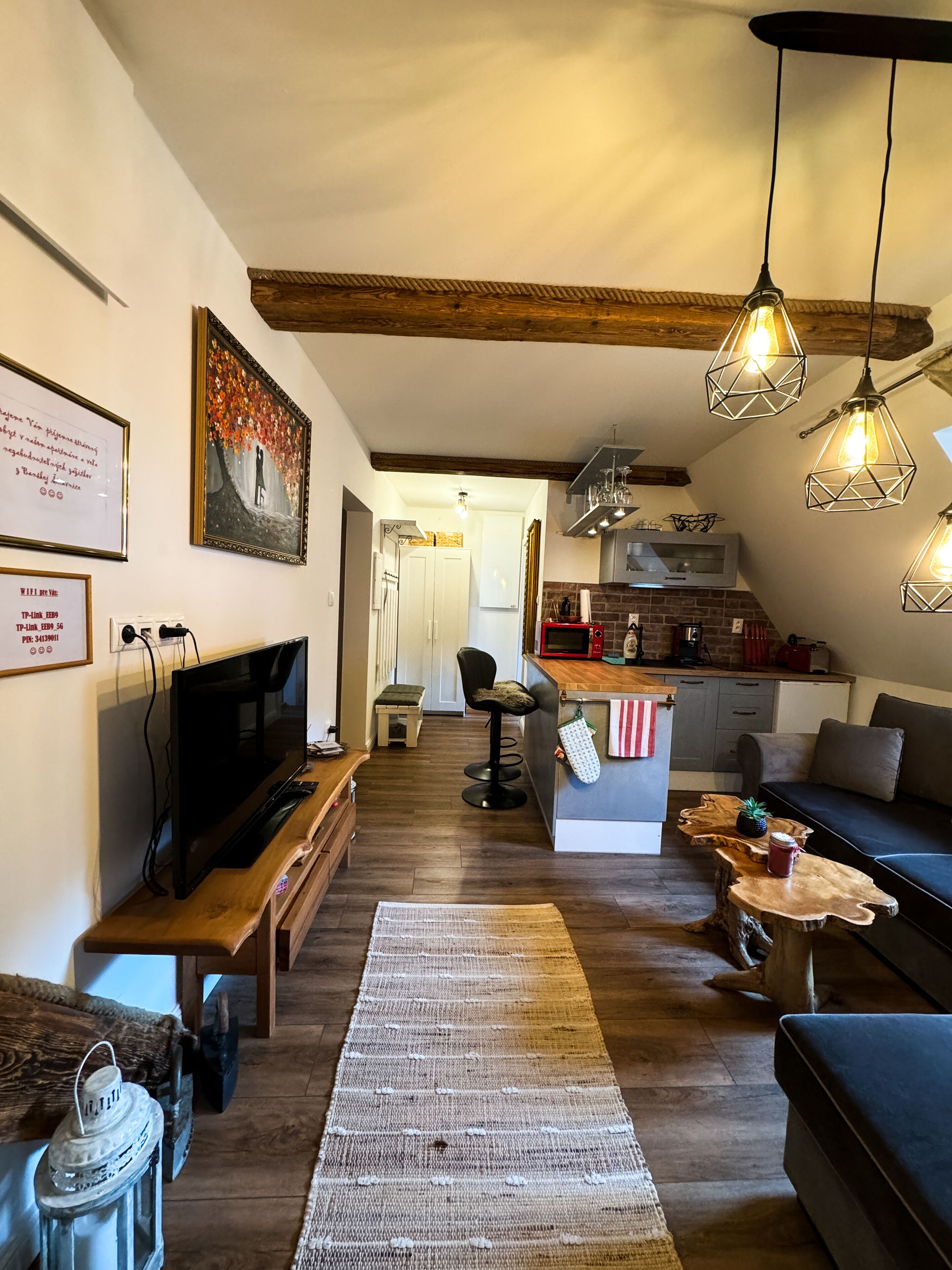 Una sala de estar acogedora con televisor, muebles de madera, alfombra y lámparas colgantes.