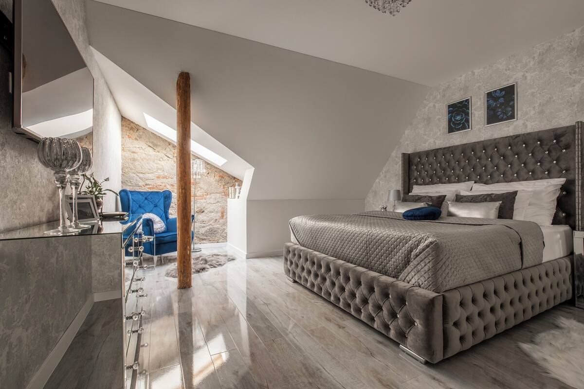 A modern bedroom with a large bed, a stone wall, and a skylight.