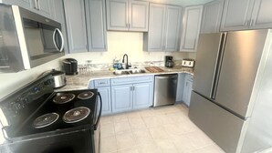 Una cocina con gabinetes grises, una estufa negra, un refrigerador de acero inoxidable y un microondas.