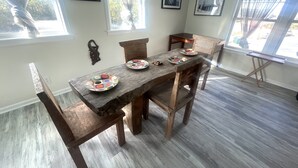 Un comedor con una mesa de madera y sillas, una mesita auxiliar y un ventanal con cortinas.