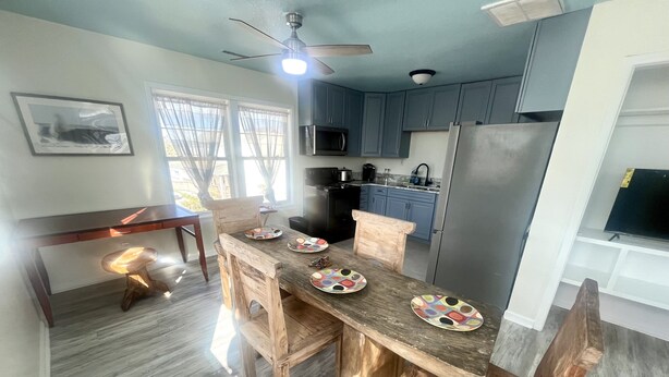 Una cocina moderna con mesa y sillas de madera, ventilador de techo y electrodomésticos integrados.