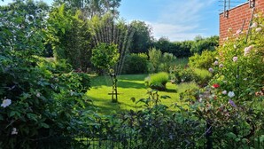 A lush garden with a variety of plants and flowers, a lawn, and a brick building with a metal structure on the roof. - Beautiful vacation apartment (1) on the north beach with WiFi for up to 4 people from 9 € pP (Putgarten)