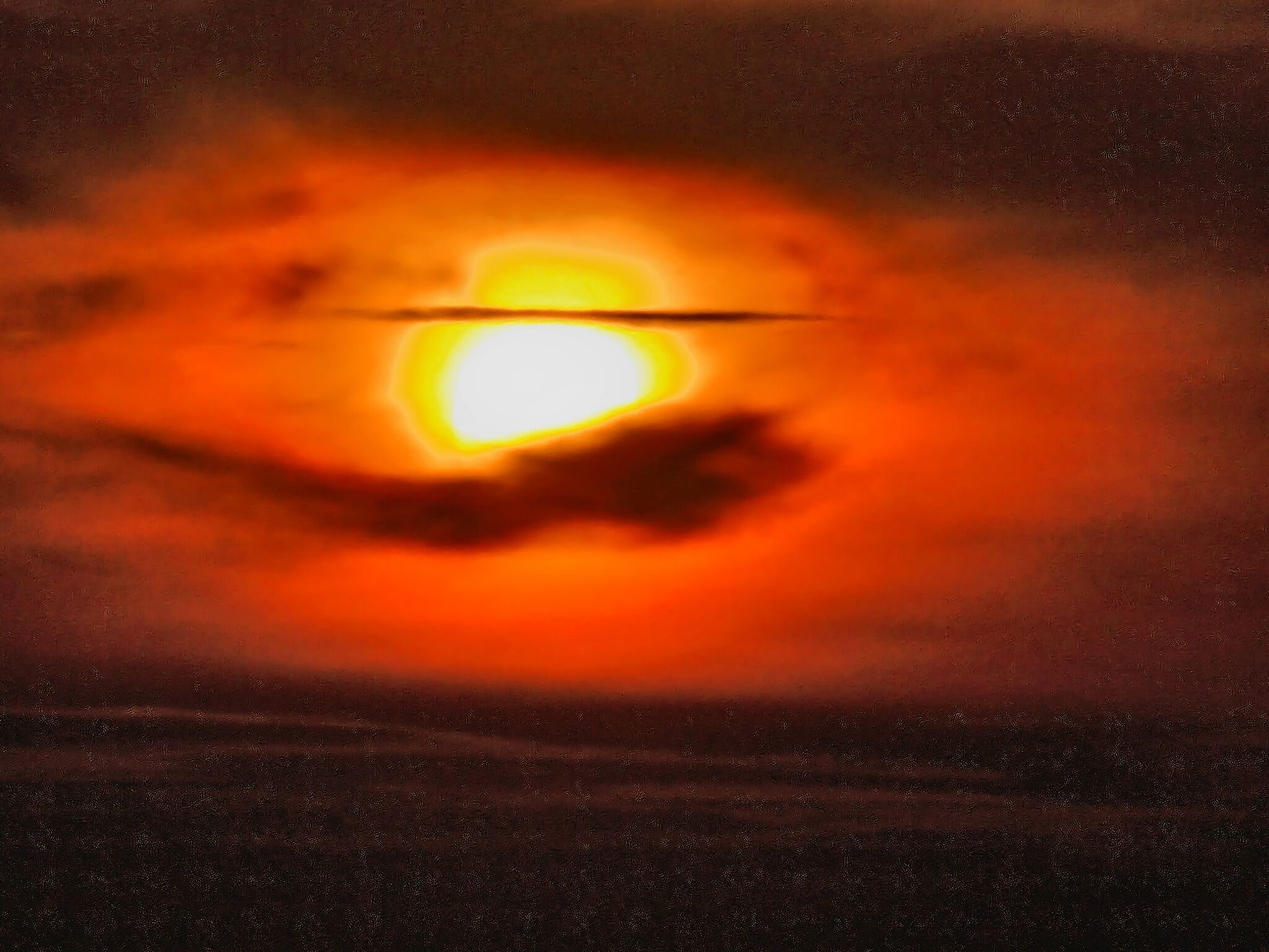 A sunset with a bright sun partially obscured by clouds.