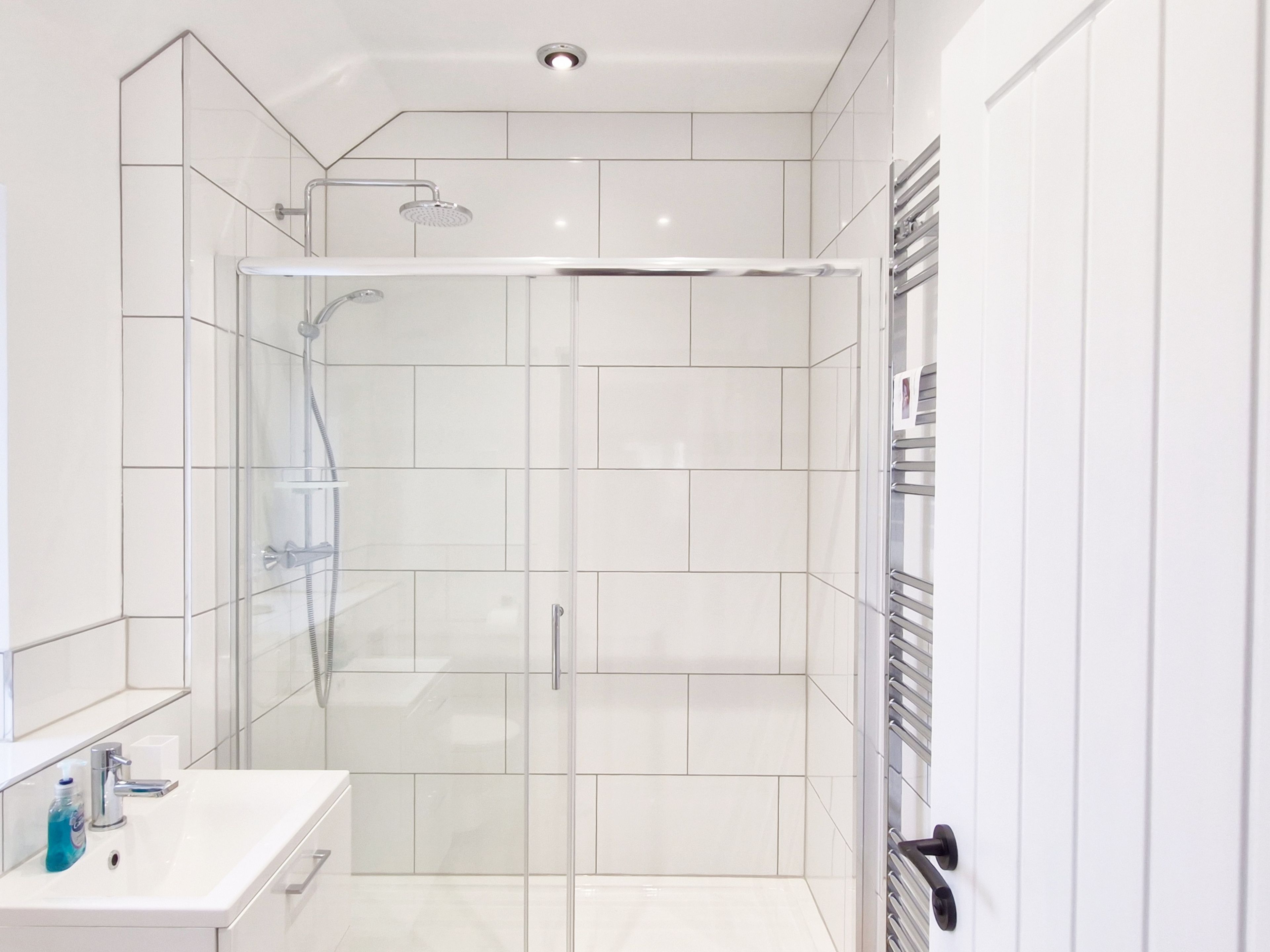 A modern bathroom with a glass-enclosed shower, white tiles, and a white sink with a mirror.