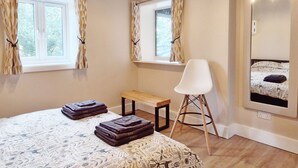 A bedroom with a bed, a bench, a chair, and two windows with curtains. - The Stables, Wickham -  a barn conversion that sleeps 2 guests  in 1 bedroom (Shedfield)