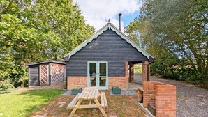 A small, dark-colored building with a sloped roof and a chimney, surrounded by a brick patio and a wooden table. - The Stables, Wickham -  a barn conversion that sleeps 2 guests  in 1 bedroom (Shedfield)