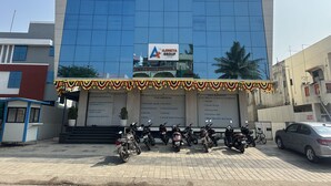 A modern building with a blue glass facade, a sign for Ajinkya Group, and several parked motorcycles. - Hotel Ajinkya Palace (Chhatrapati Sambhajinagar)