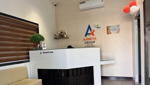 A reception area with a white reception desk, a beige sofa, a potted plant, and a wall-mounted air conditioner. - Hotel Ajinkya Palace (Chhatrapati Sambhajinagar)