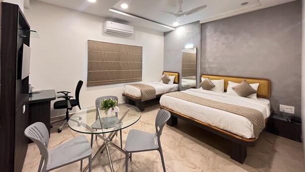 A modern hotel room with a bed, bedside tables, a desk, a glass table with chairs, and a ceiling fan. - Hotel Ajinkya Palace (Chhatrapati Sambhajinagar)