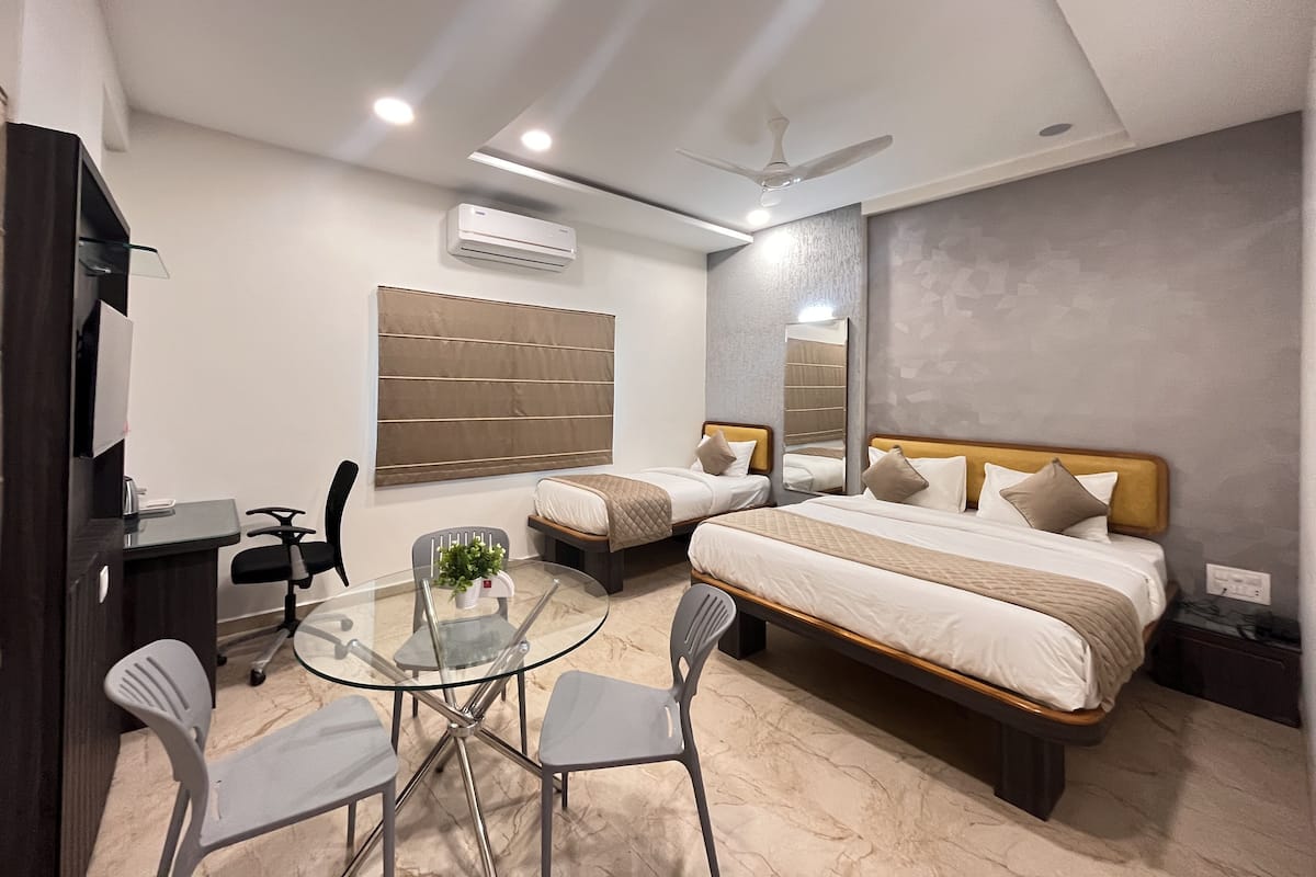 Une chambre d’hôtel moderne équipée d’un lit, de tables de chevet, d’un bureau, d’une table en verre avec des chaises et d’un ventilateur de plafond.