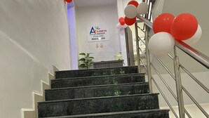 A staircase with black granite steps and metal railings, leading to a reception area with a sign for 'AJINKYA Group' and balloons. - Hotel Ajinkya Palace (Chhatrapati Sambhajinagar)