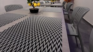 A modern dining area with a long table, patterned tablecloth, chairs, a ceiling fan, and decorative plants. - Hotel Ajinkya Palace (Chhatrapati Sambhajinagar)