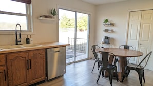 A kitchen with wooden cabinets, a dishwasher, a dining table with chairs, and a sliding glass door leading to a patio.