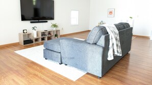 A modern living room with a grey sofa, a flat-screen TV, wooden flooring, and a white ceiling.