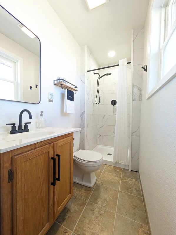 Un baño con lavamanos blanco, armarios de madera, inodoro y ducha con puerta de cristal.