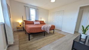A bedroom with a bed, bedside table, lamp, and a potted plant.