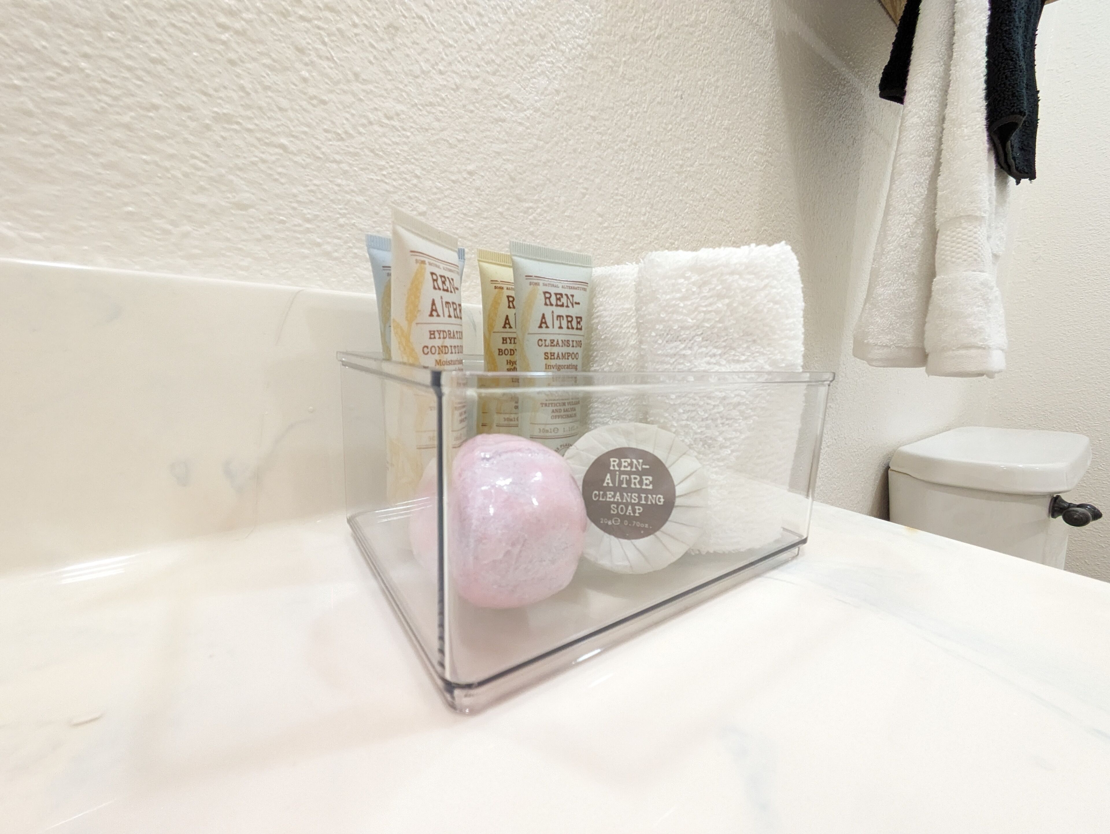 A bathroom with a glass soap dish holding a bar of Ren-Aitri cleansing soap, a pink stone, and two Ren-Aitri body lotion packets.