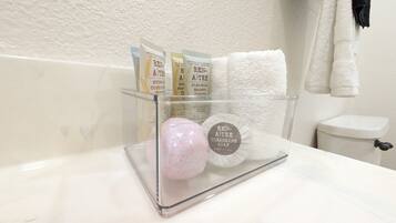 A bathroom with a glass soap dish holding a bar of Ren-Aitri cleansing soap, a pink stone, and two Ren-Aitri body lotion packets.