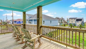 A wooden deck with rocking chairs overlooking a residential area with houses and a clear sky. - AfterDuneDelight-Fenced in yard-3 bedroom, 2 bath, sleeps 10 (Crystal Beach)