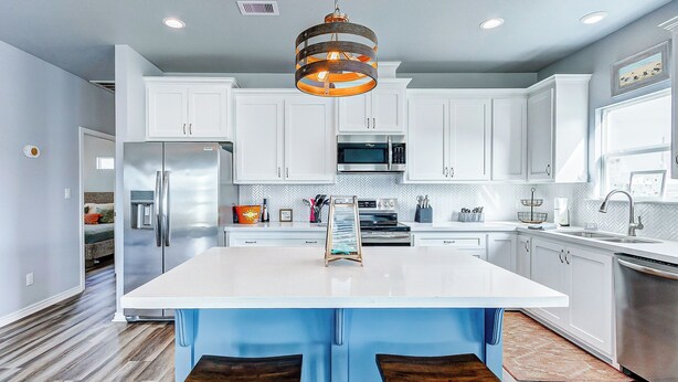 A modern kitchen with white cabinets, stainless steel appliances, and a central island with bar stools. - AfterDuneDelight-Fenced in yard-3 bedroom, 2 bath, sleeps 10 (Crystal Beach)