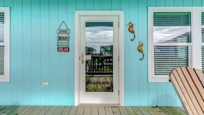 A turquoise-painted room with a door leading to a deck, a seahorse decoration, and a 'SAND BEACH RELAX' sign. - AfterDuneDelight-Fenced in yard-3 bedroom, 2 bath, sleeps 10 (Crystal Beach)