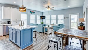 A modern kitchen with a blue island, white cabinets, and a ceiling fan. - AfterDuneDelight-Fenced in yard-3 bedroom, 2 bath, sleeps 10 (Crystal Beach)