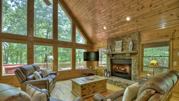 Ein gemütliches Blockhaus-Interieur mit Kamin, Ledersofas und großen Fenstern mit Blick auf den Wald.