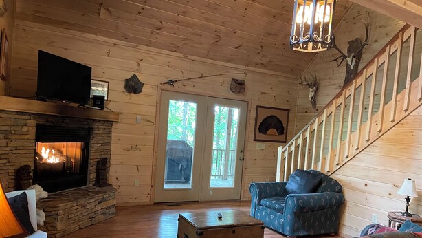 A cozy cabin interior with a stone fireplace, wooden walls, a blue patterned sofa, and a staircase. - Bucksnort Lodge- Blue Ridge GA (Blue Ridge)
