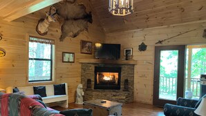 A cozy cabin interior with a stone fireplace, wooden walls, a mounted animal head, and a comfortable seating area. - Bucksnort Lodge- Blue Ridge GA (Blue Ridge)